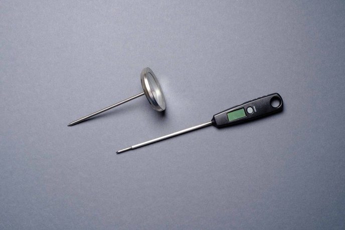 Analoges und digitales Bratenthermometer nebeneinander auf grauem Grund