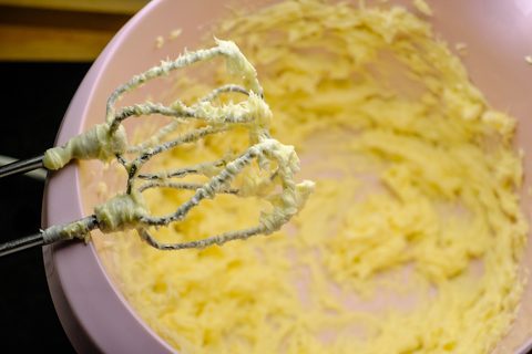 Butter wird in einer rosa Backschüssel aus Kunststoff mit dem Handrührgerät schaumig geschlagen