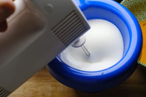 Handrührgerät schlägt Eiweiß in einer blauen Schüssel zu Eischnee