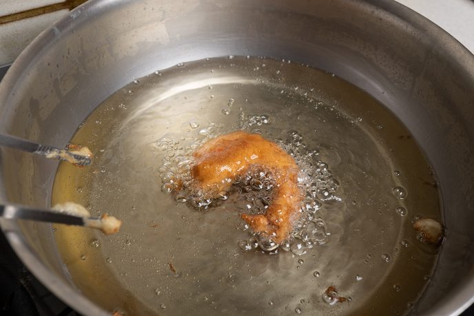 Garnele im Tempurateig wird mit einer langen Pinzette im heißen Fett gewendet