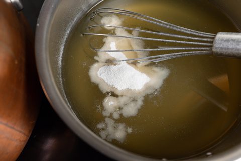 Schneebesen rührt Geliermittel in Holunderblütensirup im Topf ein