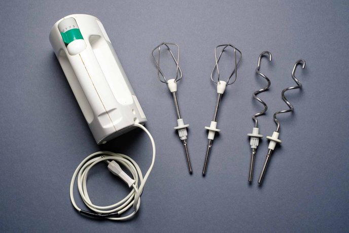 Weißes Handrührgerät mit zwei Rührbesen und zwei Knethaken auf grauem Grund