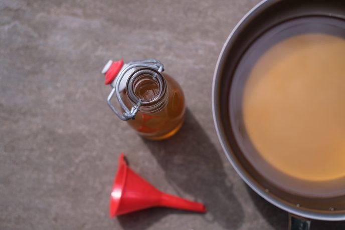 Kleine Glasflasche, roter Trichter und ein Topf mit Sirup