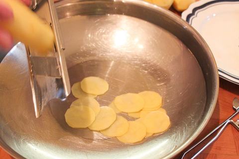 Kartoffelscheiben fallen vom Handhobel in eine Schüssel