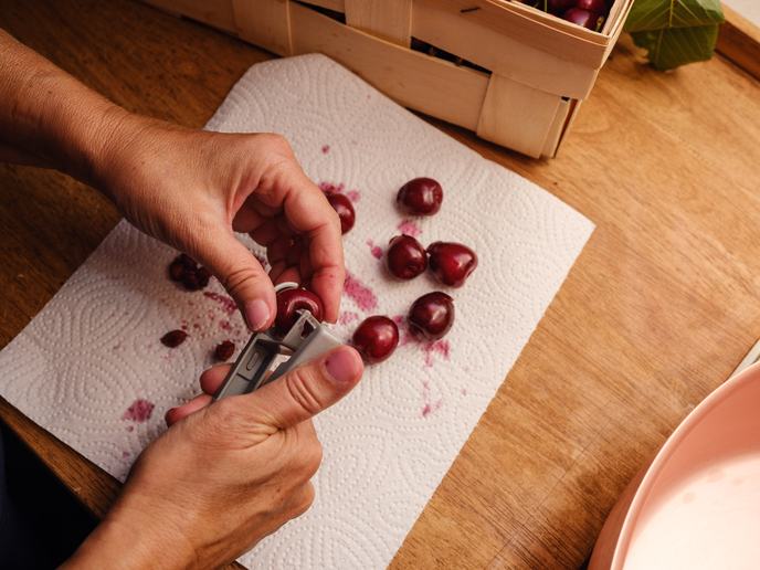 Hände entkernen Kirschen mit einem Kirschentkerner über Küchenpapier