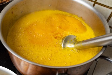 Stabmixer im Topf mit leuchtend orangefarbener Kürbissuppe