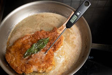 Digitales Einstichthermometer steckt in einem panierten Kalbskotelett in der Pfanne
