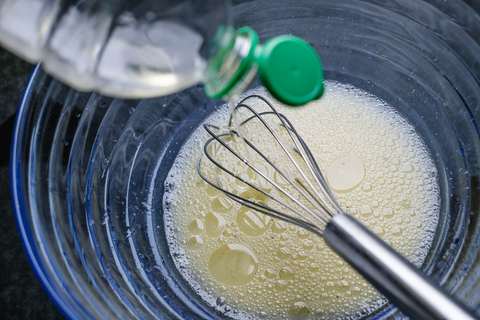 Öl wird aus einer Flasche in eine Glasschüssel gegossen und mit dem Schneebesen eingerührt