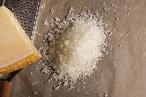 Fein geriebener Parmesan neben einem Stück Parmesan und einer Reibe