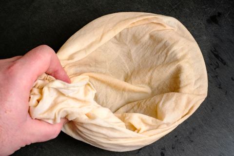 Hand legt ein helles Passiertuch aus Baumwolle in ein Sieb