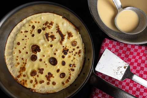 Goldbraun gebackener Pfannkuchen in der Pfanne, daneben ein Pfannenwender aus Edelstahl