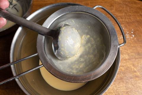 Pfannkuchenteig wird mit einer Kelle durch ein Haarsieb gestrichen