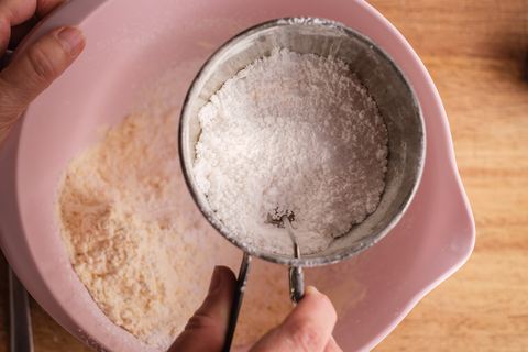 Puderzucker im Bechersieb über einer rosa Rührschüssel