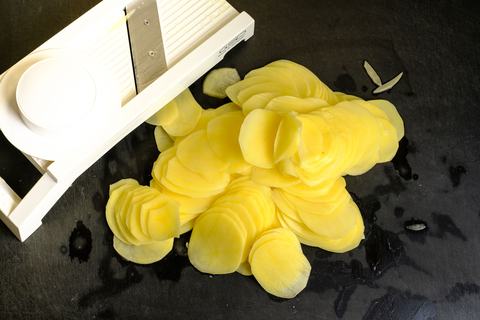 Rohe Kartoffeln in dünne Scheiben gehobelt neben dem weißen Gemüsehobel