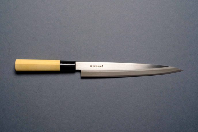 Sashimi-Messer mit langer, schmaler Klinge und hellem Holzgriff auf grauem Grund