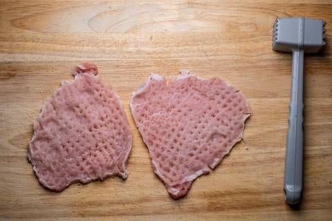 Zwei geklopfte Schnitzel auf dem Holzbrett, daneben ein Fleischklopfer