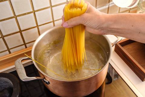 Spaghetti werden in kochendes Wasser im Kupfertopf gegeben