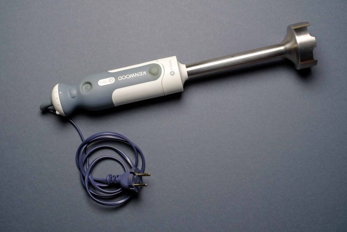 Stabmixer mit Edelstahlfuß und Kabel auf grauem Grund